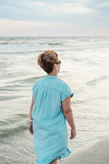 Senior woman relaxing on beach on sunset. Thoughtful mature woman day dreaming at beach. Summer, vacation, holiday, active retired people. Older female travelling at holiday.