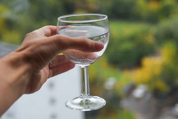 Glass with water in a woman's hand on the background of a summer landscape. Summer. Health. Useful habit. Drinking water. beautiful photo. Pure water