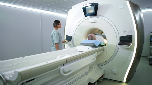Magnetic resonance imaging in the modern hospital, young woman doctor performs a magnetic tomographic examination of a elderly man, MRI, modern technologies in medicine, end of the procedure.