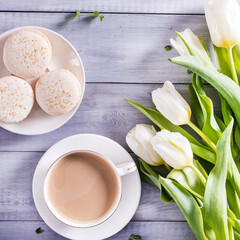 Morning cup of coffee, cake macaron and spring tulip whate flowers on white wooden background. Flat lay.Beautiful breakfast for Women