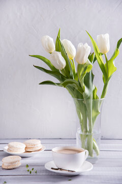Morning cup of coffee, cake macaron and spring tulip whate flowers on white wooden background. Beautiful breakfast for Women
