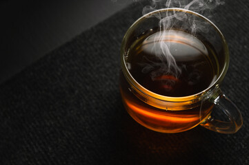 Hot black tea in a transparent cup on a black background