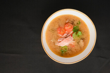 Vegetable soup with salmon in white bowl over black background. Dinner concept, healthy hot soup.