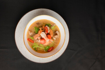 Broth soup with seafood. Shrimps and clams soup served in a white bowl over black background.