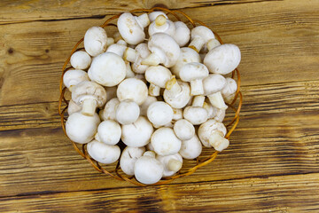 Fresh champignon mushrooms in wicker basket on the wooden table. Top view