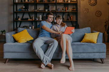 Couple on sofa having video call. Man and woman in headphones speaking with relatives through tablet.
