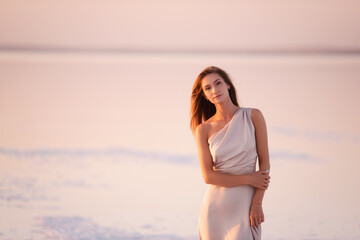 Fototapeta na wymiar Portrait of a young blonde woman in an evening airy pastel pink, powdery dress against a background of beautiful sunset. Girl with natural make-up, hair grows through the air. Copy space