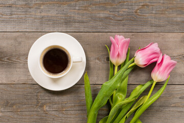Obraz na płótnie Canvas fresh pink tulips on gray wooden aged table top, good morning or greetings bouquet with white coffee cup