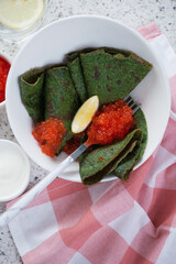 Green crepes with addition of spinach and red caviar in a white bowl, vertical shot, above view