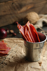 Homemade beef jerky seasoned with garlic, onion, pepper and salt. Jerky in a bucket on a wooden...