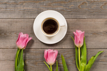 fresh pink tulips on gray wooden aged table top, good morning or greetings bouquet with white coffee cup