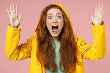 Close up redhead young angry shocked woman in yellow waterproof raincoat outerwear hood spread hands shout scream isolated on pastel pink background studio Outdoors wet weather fall season concept