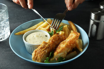 Female hands hold cutlery over the fried fish and chips, close up