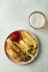 Plate with fried fish and chips, and beer on white textured table
