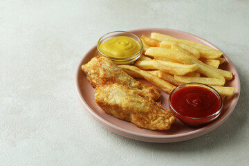 Plate with fried fish and chips, and sauces on white textured background