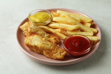 Plate with fried fish and chips, and sauces on white textured background