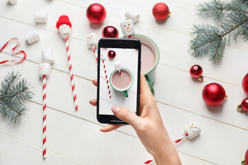 Female food photographer with mobile phone taking picture of tasty cacao drink with marshmallows, top view