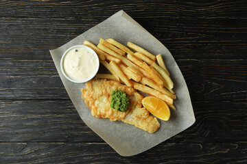 Baking paper with fried chips and fish on wooden background