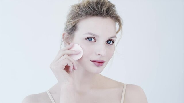 Young woman takes care of her face. Cotton disk. Gentle skin care. Clean smooth skin. Girl on white background. Advertising of natural cosmetics. Cosmetic disc for make-up removal. Hygiene product.
