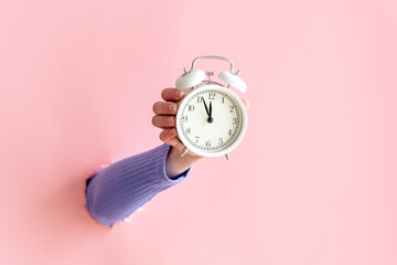 female hand hold vintage white alarm clock on pink background.