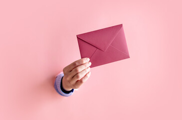 female hand hold red envelope on pink background.