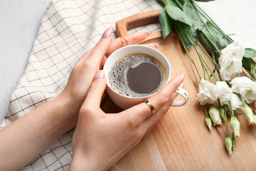 Female hands with cup of coffee and spring flowers on light background