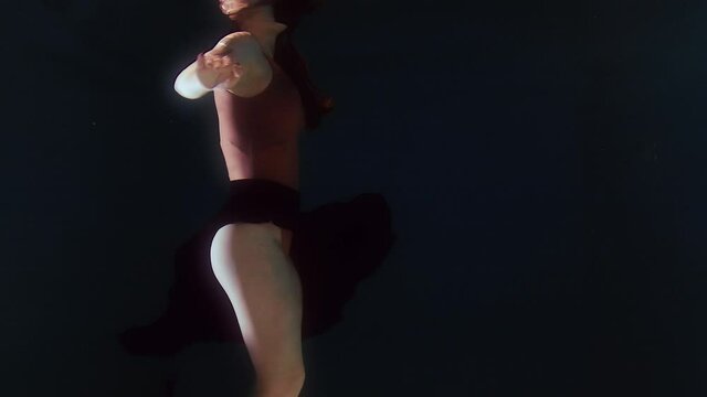 Woman in a swimsuit and a black skirt swims in the water, waving arms and legs. Shooting underwater.
