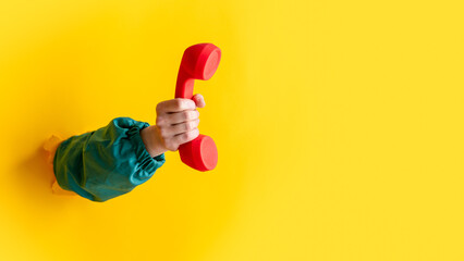 female hand hold classic red handset on yellow background.