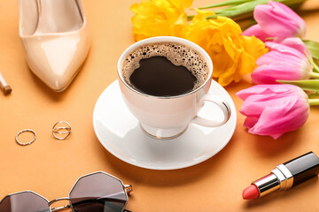 Cup of coffee with flowers and female accessories on color background