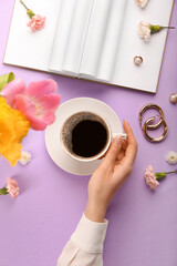 Female hand with cup of coffee and spring flowers on color background