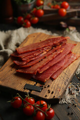 Delicious smoked sausage on a dark wooden board with tomatoes and spices. Delicious handmade snack...