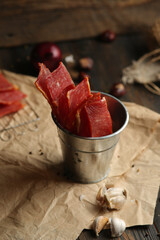 Homemade beef jerky seasoned with garlic, onion, pepper and salt. Jerky in a bucket on a wooden...
