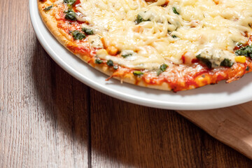 Cooked pizza with cheese and chicken pieces. Close up. Italian style meal. Fast food product on a wooden table surface.
