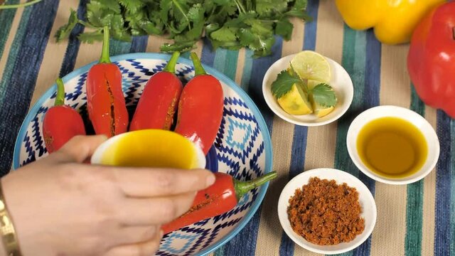 Female pouring mustard oil on spicy stuffed red chili pickle kept on a plate. Closeup shot of Rajasthani Mirchi Achaar with oil  lemon pieces  Masala  coriander leaves  and bell peppers on a table
