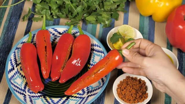 Female keeping a stuffed red chili pickle with other chilies on the table. Closeup shot of a bowl of Masala  lemon slices  mustard oil  and coriander with Indian Mirchi Achaar