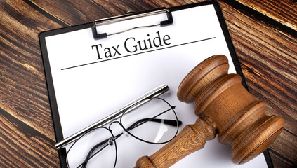 Paper with TAX GUIDE with gavel, pen and glasses on wooden background