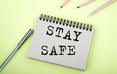 STAY SAFE text on the notebook with pen on yellow background