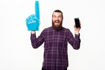 Amazed and joyful young man in casual pointing with fan glove and showing smartphone