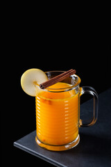 A glass of sea buckthorn tea with slice of pear and cinnamon stick on black background. Prevention of colds, strengthening the immune system. Copy space.