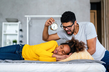 Father of black ethnicity waking up daughter for school with alarm clock