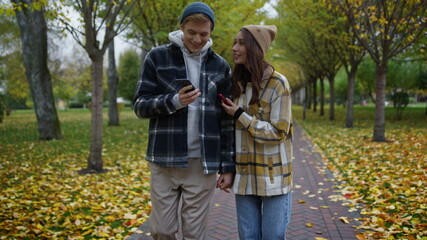 Fototapeta premium Close up of smiling young couple looking smartphones in autumn park. 