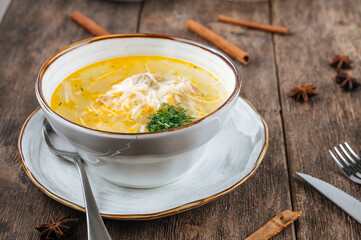 A bowl of chicken noodle soup with greens on the wooden background