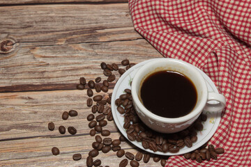 hot coffee cups and coffee beans and red plaid cloth on a wooden background.