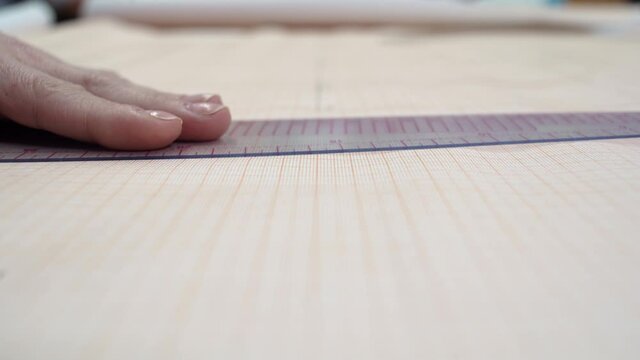 close-up of a female hand applies a ruler to graph paper and draws a line. clothing designer concept.