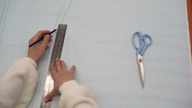 top view of a female hand applies a ruler to graph paper and draws a line. clothing designer concept.