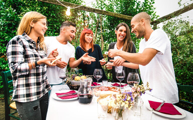 Young people having fun eating local food and drinking red wine at country side garden fest - Friendship and life style concept with happy friends together at farmhouse patio party - Warm vivid filter