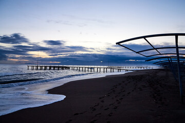 View from beach to water of sea, waves with white foam, pierce and sky with clouds in a nice evening.