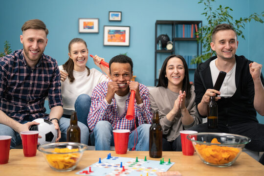 Zoom in of multi-ethnic group of friends celebrating victory of their team. They yelling, clapping hands and whistling while sitting in living room and watching TV match