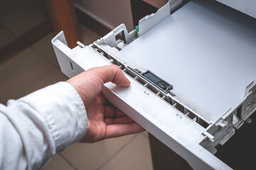 Working with an office printer: Male hand closes the printer's paper tray. Loading paper in the...