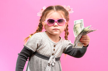 Little girl in glasses with a package and money on a pink background, child and shopping.